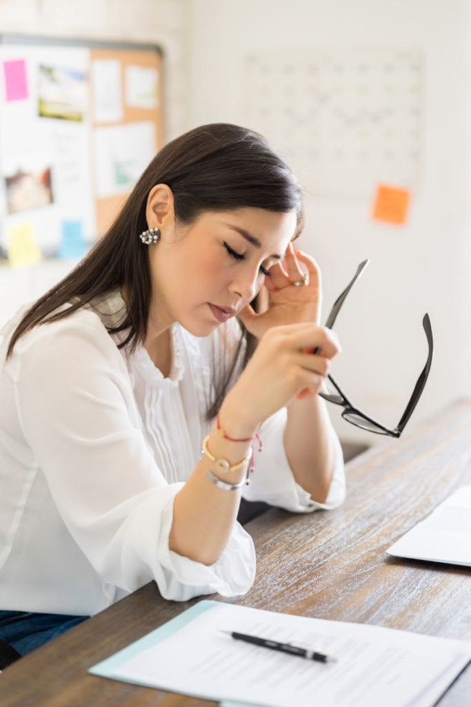 Woman looking stressed at work holding her glasses with eyes closed